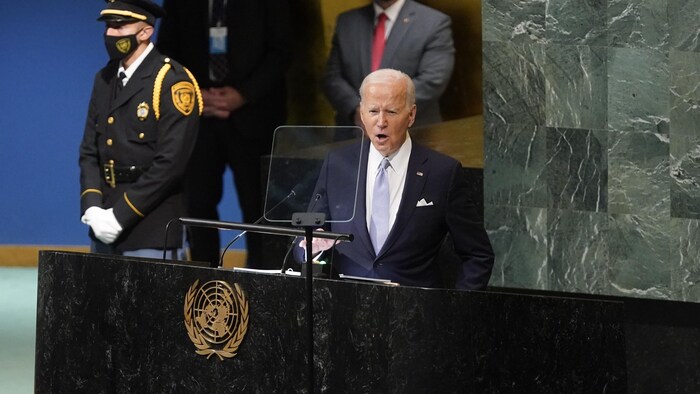 Joe Biden parle devant un lutrin aux Nations unies, près d'un garde en uniforme.
