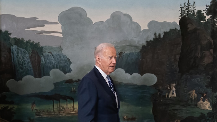 Joe Biden marche devant une grande murale peinte.