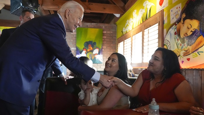 Dans un restaurant, Joe Biden serre la main de deux jeunes femmes dont l'une tient dans ses bras un jeune enfant.
