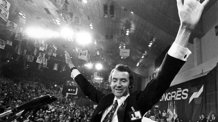 Joe Clark tend les bras au ciel devant une foule.