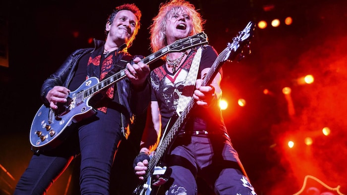 Le guitariste et le bassiste de Def Leppard, sur scène, sourient en regardant la foule.