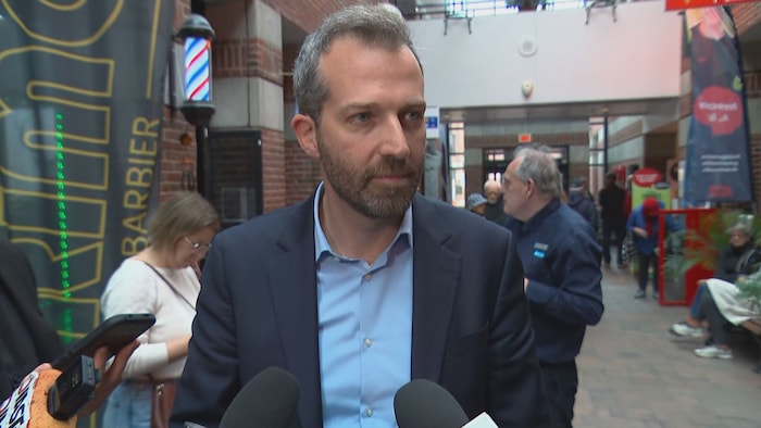 Joël Lightbound donne une entrevue à des journalistes dans une halle.