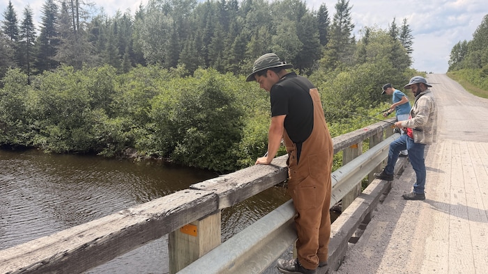 Deux hommes et un adolescent pêchent sur un pont.