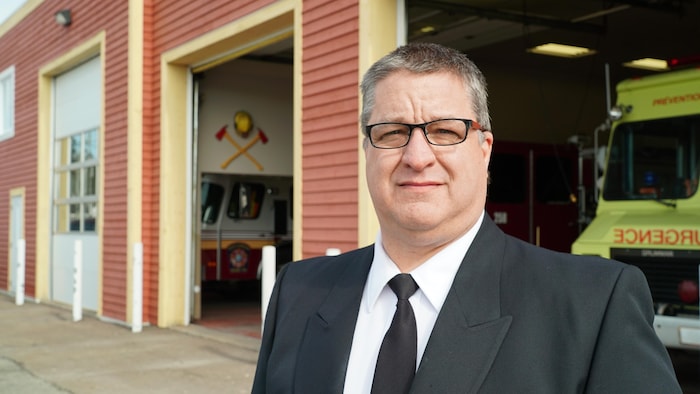 Le directeur des services incendie de la Ville de Sept-Îles, Joël Sauvé, souriant devant une caserne de pompiers.