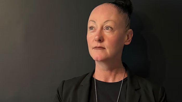 Une femme vêtue de noir porte un insigne de la GRC autour du cou. Une veste pare-balles portant l'inscription « POLICE » est posée devant elle.