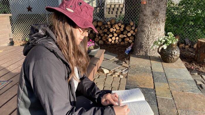 L'autrice Joëlle Préfontaine assise sur les marche d'une terrasse en bois, en train d'écrire.