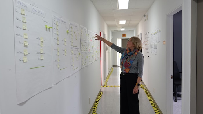 Johanne Côté pointe un mur rempli de feuilles de papier et petites notes.