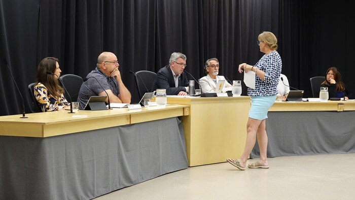 Une dame avec une lettre en main, devant la table du conseil municipal.