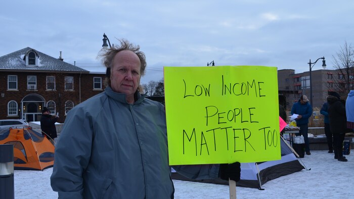 Un homme tenant une pancarte sur laquelle il est écrit en anglais «Les personnes à faible revenu compte aussi ».