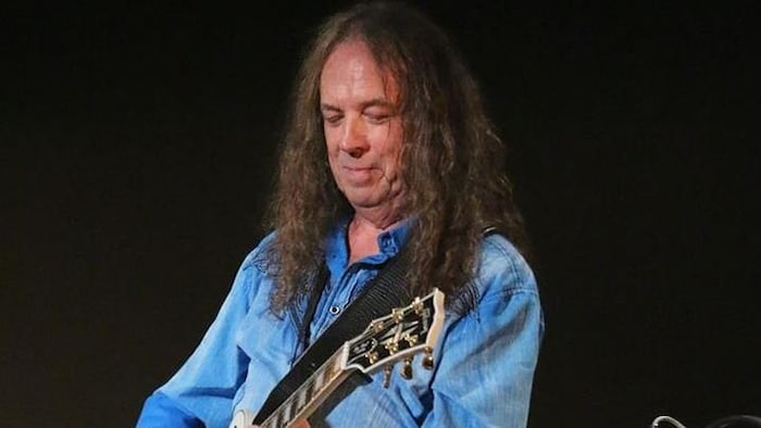 Un homme tient une guitare sur scène.