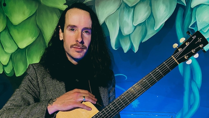 John McLaren pose en tenant une guitare. 