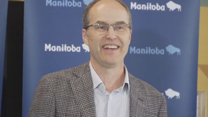John Pollard devant un rideau bleu sur lequel les mots Manitoba et des bisons sont imprimés.