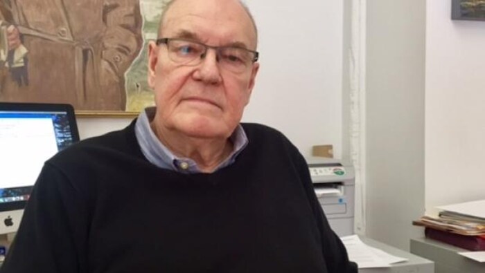 Un portrait du coordonnateur de la Coalition torontoise sur la responsabilisation de la police, John Sewel devant son bureau. Il porte des lunettes et est âgé de 77 ans.