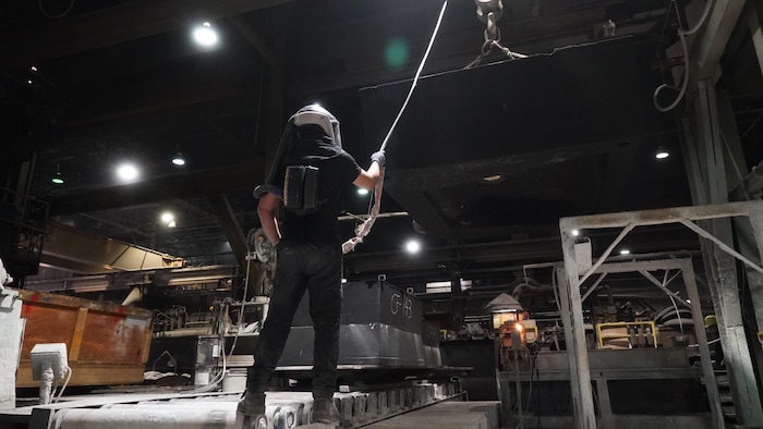 Un homme en noir avec un casque de dos tient un câble dans une usine.