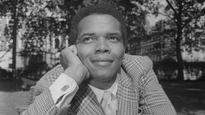 Une photo datant des années 1960 montre le chanteur participant à une séance de photos, assis sur un banc de parc à l'extérieur.