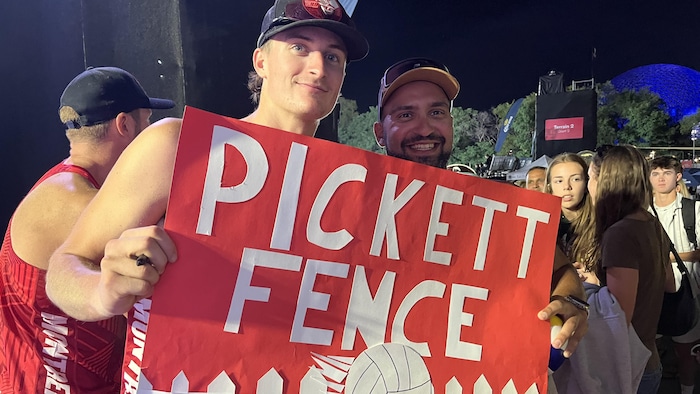 Le volleyeur tient une pancarte sur laquelle il est écrit Pickett Fence (la clôture Pickett), à côté d'un amateur souriant.