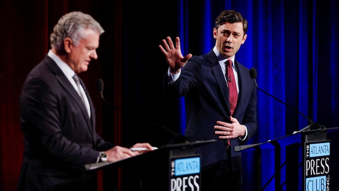 Mike Collins consulte ses notes à un pupitre tandis que Jon Ossoff s'exprime la main levée, en le regardant.
