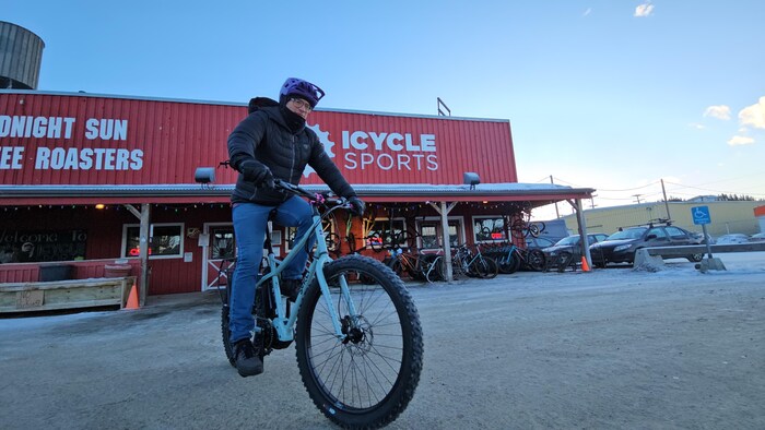 Un homme chevauche un vélo électrique devant un magasin de vélo.