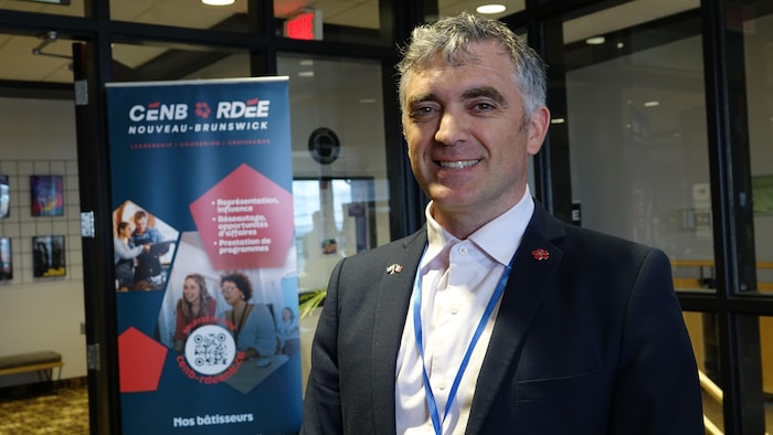 Un homme avec un tailleur regarde l'objectif en souriant, devant un panneau du Conseil économique.