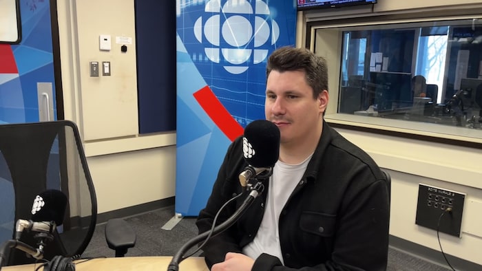 Un homme est assis devant un micro dans un studio de radio.