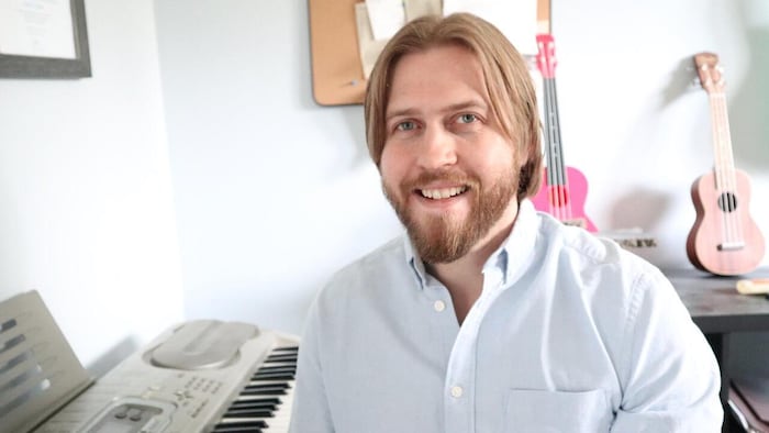 Jordan Laidlaw est assis à un piano et sourit à la caméra.