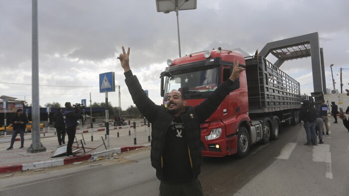 Un homme sourit et brandit les bras en signe de victoire devant un camion traversant un point de passage.