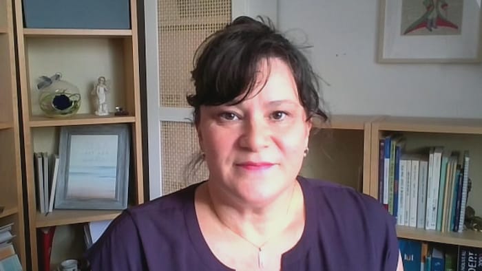 Capture d'écran d'une entrevue en visioconférence avec Josée Beaudoin. Dans un bureau où se trouvent des livres et des bibelots disposés dans des bibliothèques derrière elle, Madame Beaudoin fixe directement la caméra.