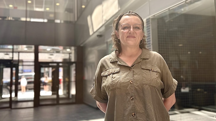 Debout, les mains derrière le dos, Josée Larouche sourit à la caméra, dans un atrium inondé de lumière naturelle.