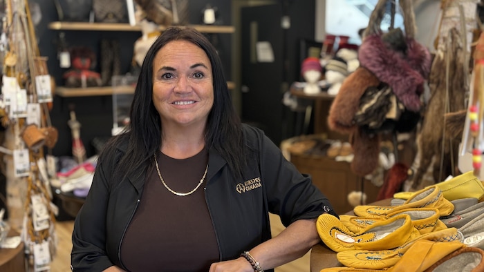 Une femme aux cheveux mi-longs sourit face à la caméra. Elle porte une veste sombre brodée du logo Atikuss Canada et une chaîne fine.