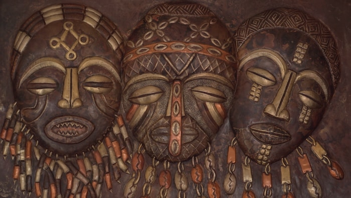 Un tableau en cuivre martelé qui représente des masques de cérémonie congolais.