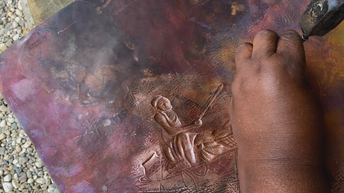 L'artiste Joséphine Tambwe Feza Kabibi travaille une oeuvre en cuivre martelé intitulée Voyage en pirogue. 