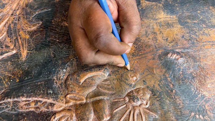 L'artiste Joséphine Tambwe Feza Kabibi trace au crayon le dessin qu'elle va sculpter dans son oeuvre en cuivre.