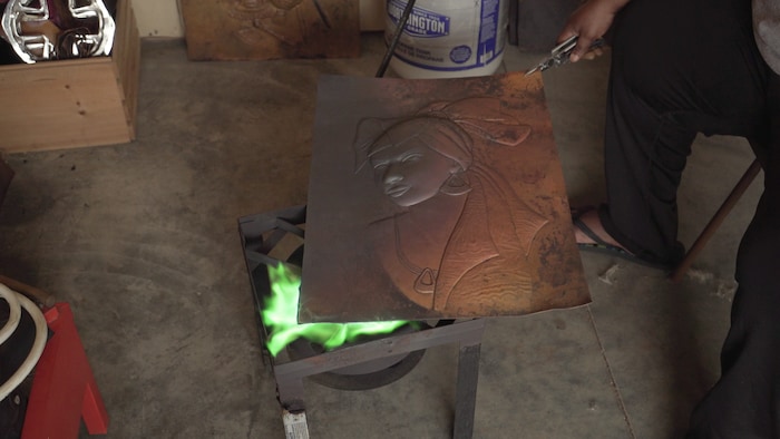 L'artiste Joséphine Tambwe Feza Kabibi doit chauffer son oeuvre de cuivre pour qu'il soit plus facile à marteler.
