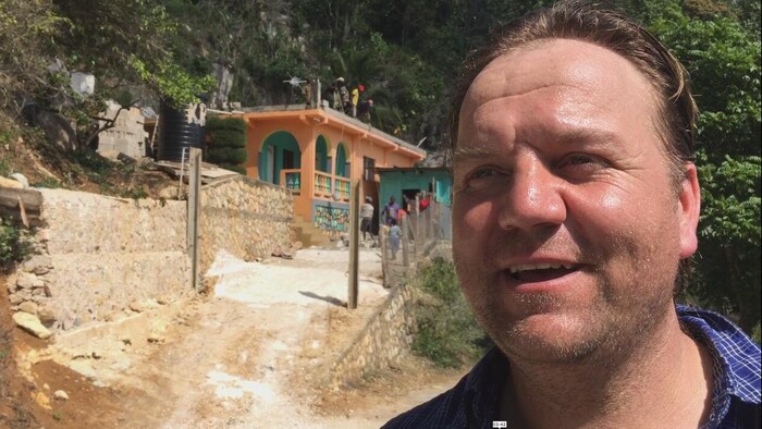 Un homme à l'extérieur aide à rénover un bâtiment, dans un décor tropical.