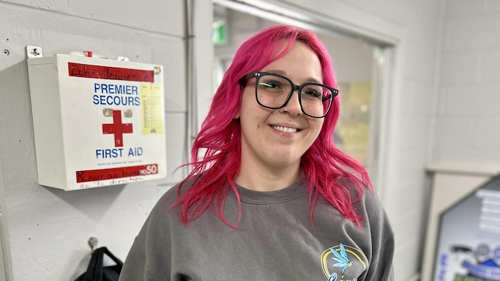 Une femme aux cheveux roses debout devant une trousse de premiers soins accrochée au mur.