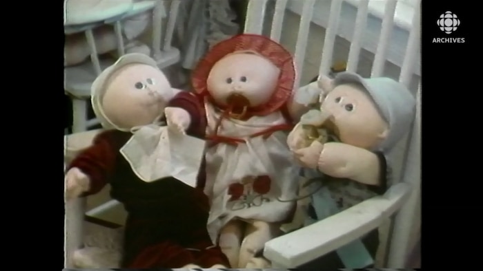 Trois poupées Bout d'chou sont assises sur une chaise berçante.