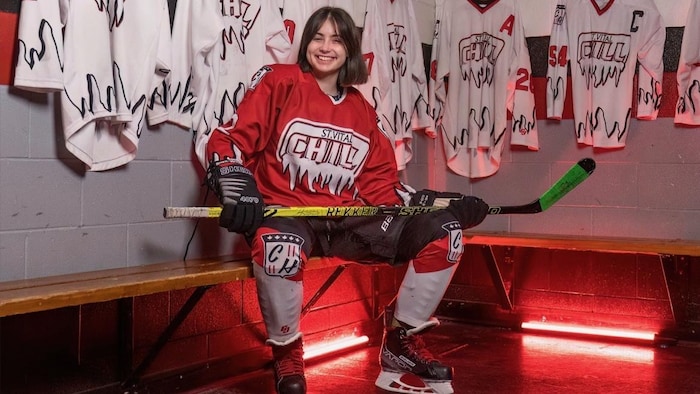 Une fille en équipement de hockey dans un vestiaire.