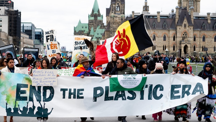 Des manifestants devant le parlement canadien marchent derrière une banderole sur laquelle on peut lire, en anglais, « Mettons fin à l'ère du plastique ».