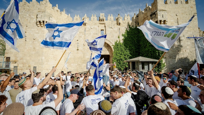 Des dizaines d'hommes formant en foule compacte sont rassemblés devant la porte de Damas et célèbrent en agitant de grands drapeaux d'Israël.