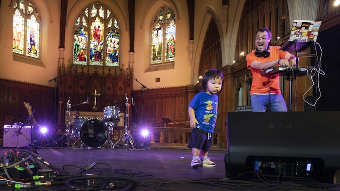 Un DJ derrière des platines et un enfant devant lui. En arrière-plan, le chœur d'une église et des vitraux.