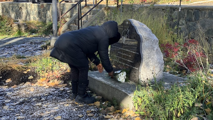 Une dame dépose un bouquet de fleurs au bas d'une dalle.