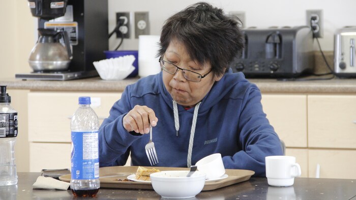 Une femme assise à une table, une fourchette en main, en train de manger.