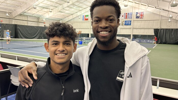 Les deux hommes sourient à la caméra en se prenant par l'épaule.