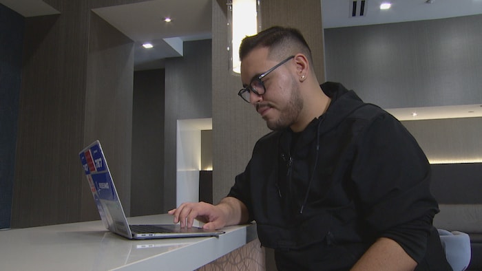 Un jeune homme portant des lunettes devant un ordinateur portable.