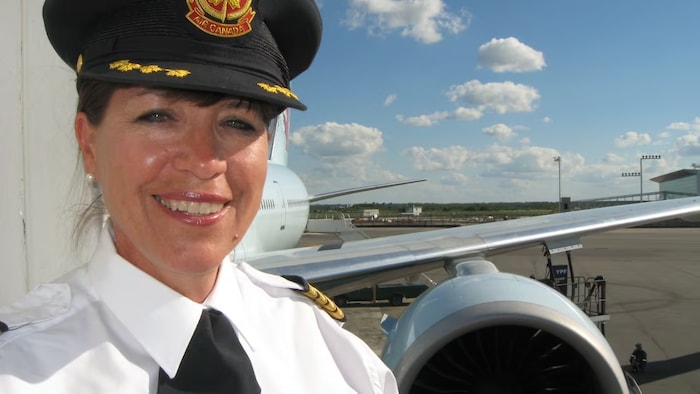 Jodi Cameron wears a pilot's uniform and smiles in front of the plane.