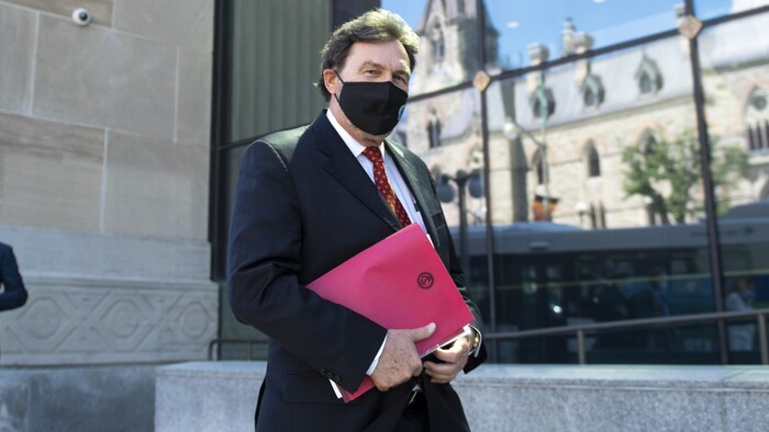 Un homme portant un couvre-visage photographié à l'extérieur d'un immeuble à la façade vitrée.