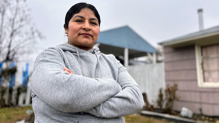 Une femme se tient debout les bras croisés, à l'extérieur de sa maison.