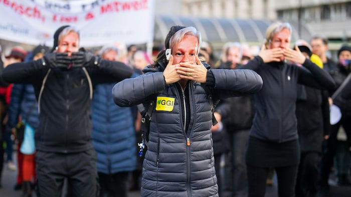 Des manifestants, les mains devant la bouche, ont tous un masque représentant le visage de Julian Assange. 