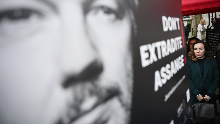 Sa femme passe devant une affiche géante de Julian Assange. 