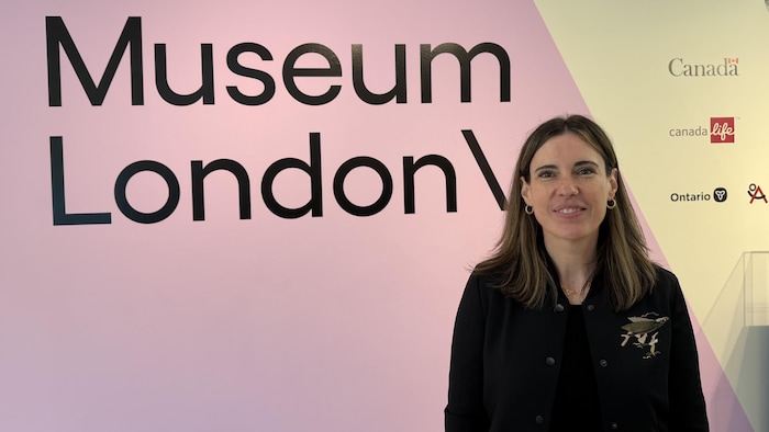 Julie Bevan, directrice générale de Museum London, se tient devant un mur rose et blanc sur lequel est inscrit « Museum London ».